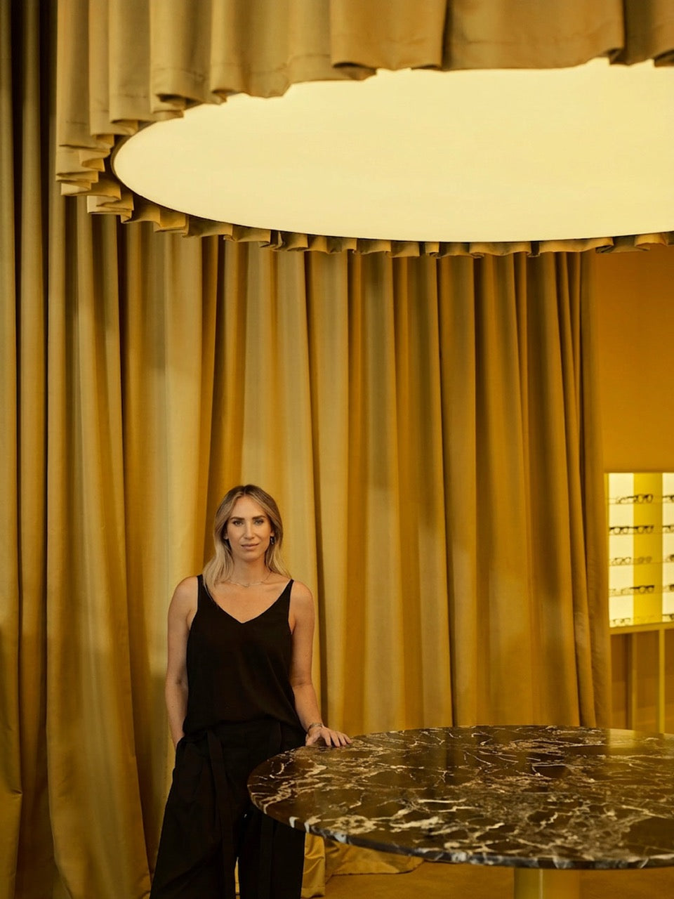 Dr Natalie Boffa standing in front of a large round light fixture with gold curtains in the background